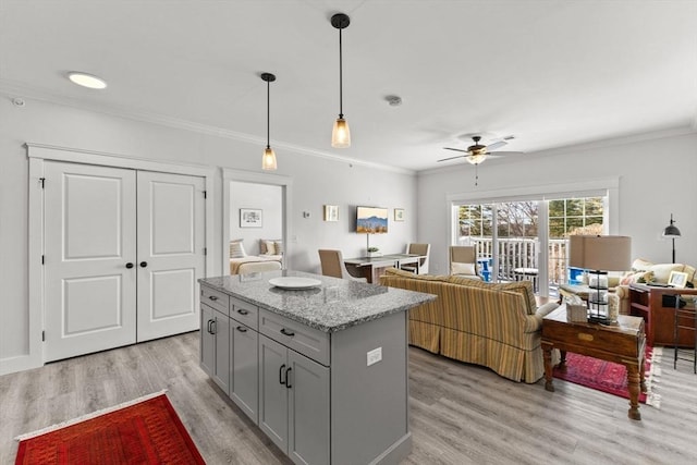 kitchen with crown molding, hanging light fixtures, a kitchen island, light stone countertops, and light hardwood / wood-style floors