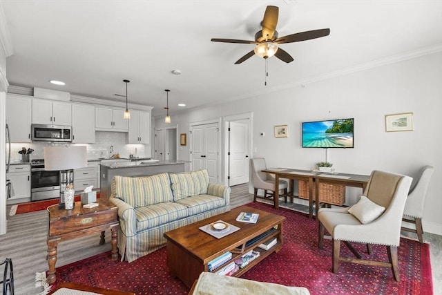 living room with crown molding, wood-type flooring, sink, and ceiling fan