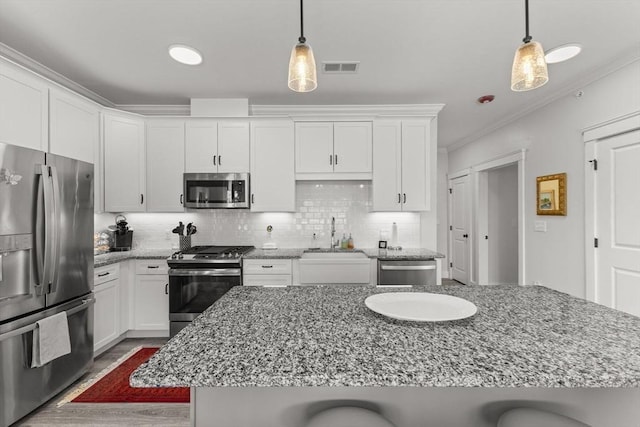 kitchen with appliances with stainless steel finishes, pendant lighting, white cabinetry, a breakfast bar area, and crown molding