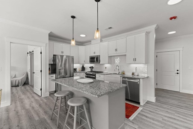 kitchen featuring appliances with stainless steel finishes, white cabinets, ornamental molding, a center island, and light stone countertops