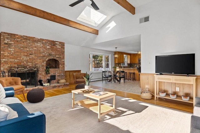 living room with a high ceiling, ceiling fan, a brick fireplace, beam ceiling, and light hardwood / wood-style flooring