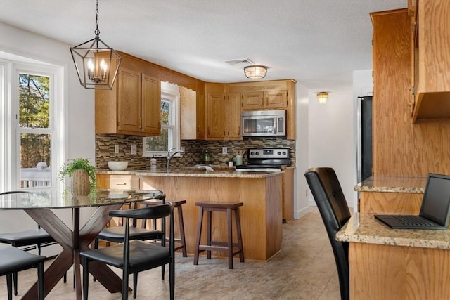 kitchen featuring kitchen peninsula, pendant lighting, stainless steel appliances, light stone countertops, and backsplash