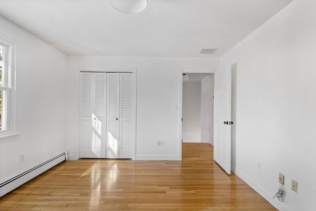 unfurnished bedroom with multiple windows, light wood-type flooring, a closet, and baseboard heating