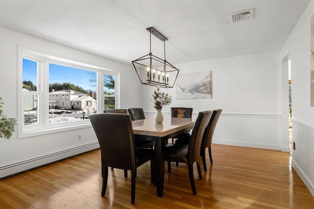 dining room with a baseboard heating unit, hardwood / wood-style floors, and a notable chandelier