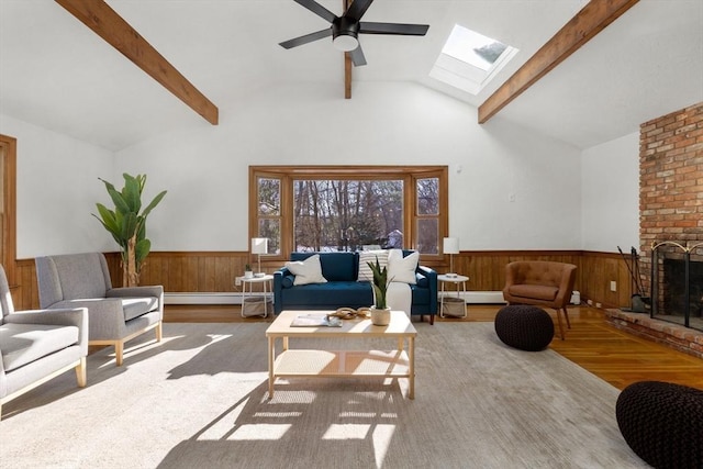 living room with ceiling fan, a fireplace, light hardwood / wood-style floors, and vaulted ceiling with skylight