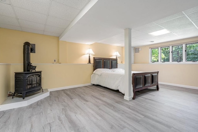 unfurnished bedroom with a paneled ceiling, a wood stove, and light hardwood / wood-style flooring