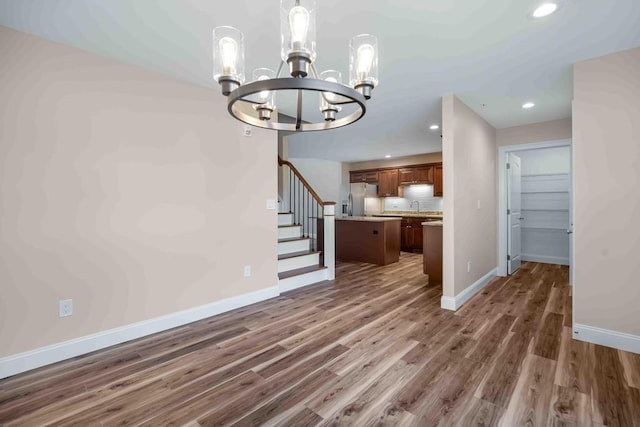 unfurnished dining area featuring baseboards, an inviting chandelier, stairs, a sink, and wood finished floors