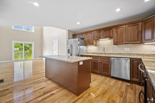 kitchen with light stone counters, a kitchen island, appliances with stainless steel finishes, light wood finished floors, and a sink