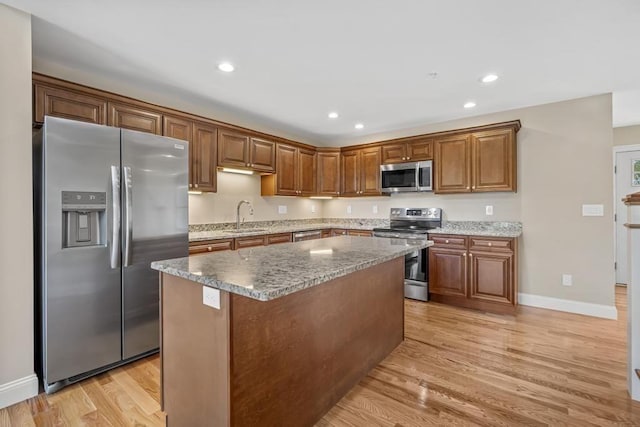 kitchen featuring baseboards, a kitchen island, light wood-style floors, stainless steel appliances, and a sink
