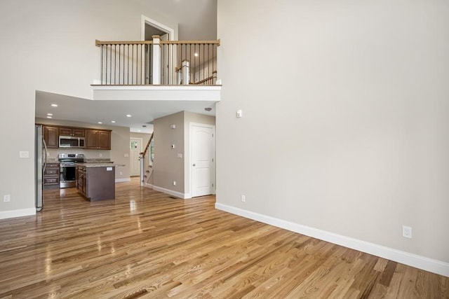 unfurnished living room featuring a high ceiling, light wood finished floors, baseboards, and stairs