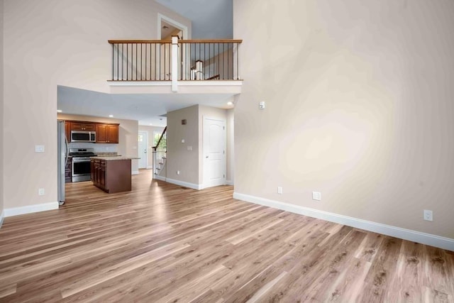 unfurnished living room featuring baseboards, light wood finished floors, a towering ceiling, and stairway