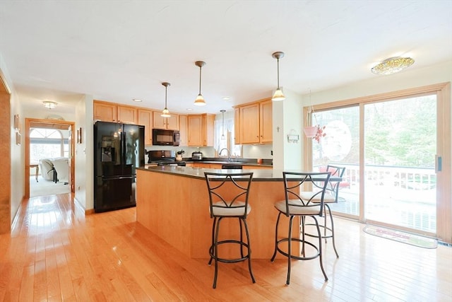 kitchen featuring light wood-style floors, dark countertops, black appliances, and light brown cabinetry