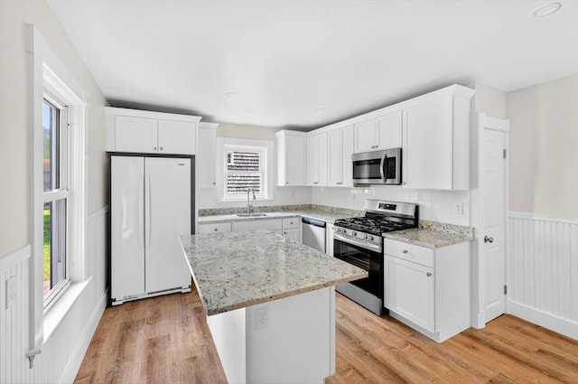 51 Ryder St, Dartmouth, MA 02747 - kitchen with stainless steel appliances, a wainscoted wall, light wood-style floors, a kitchen island, and white cabinets