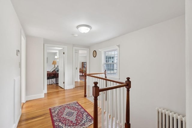 hallway with an upstairs landing, radiator, light wood-style floors, and baseboards