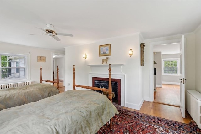 bedroom with radiator, wood finished floors, a fireplace, ornamental molding, and baseboards