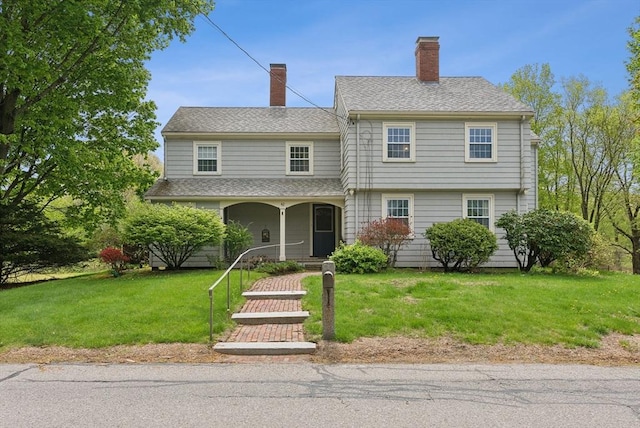 colonial inspired home featuring covered porch, a front lawn, and a chimney
