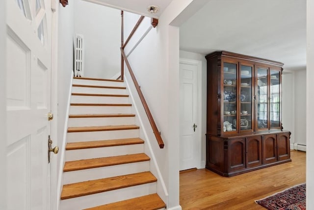 stairs featuring a baseboard heating unit and wood finished floors