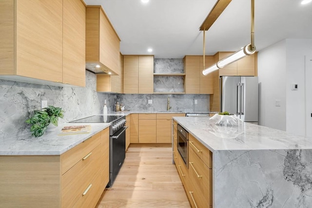 kitchen with sink, light wood-type flooring, a kitchen island, stainless steel appliances, and light stone countertops