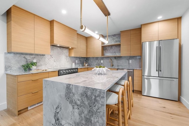 kitchen with premium range hood, appliances with stainless steel finishes, a center island, light hardwood / wood-style floors, and light stone countertops