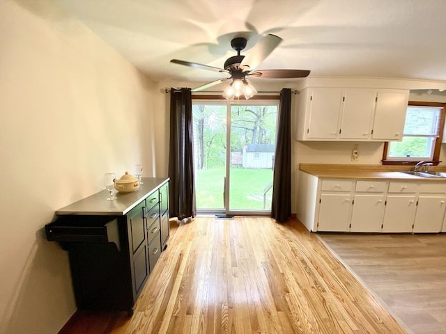 kitchen featuring white cabinets, light wood-style floors, light countertops, ceiling fan, and a sink