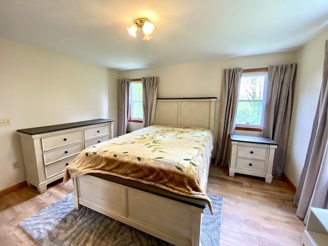 bedroom with multiple windows, light wood-style floors, and baseboards