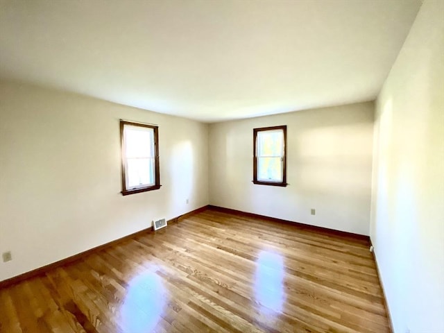 unfurnished room featuring healthy amount of natural light, wood finished floors, and baseboards