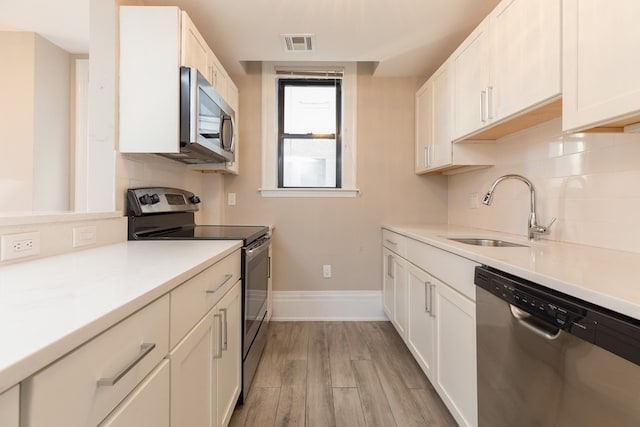 kitchen with white cabinetry, sink, appliances with stainless steel finishes, tasteful backsplash, and light wood-type flooring