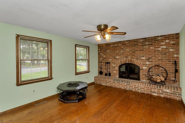 unfurnished living room featuring wood finished floors, ceiling fan, baseboards, a fireplace, and a textured ceiling