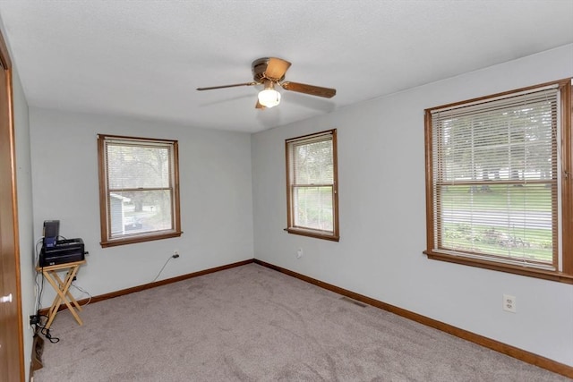 spare room featuring healthy amount of natural light, light colored carpet, a ceiling fan, and baseboards