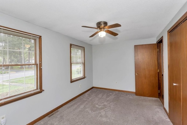unfurnished bedroom featuring light carpet, baseboards, a closet, and ceiling fan