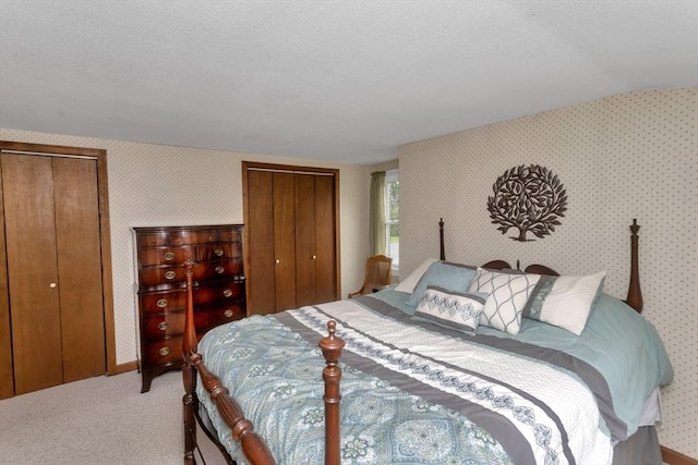 bedroom with wallpapered walls, multiple closets, carpet flooring, and lofted ceiling