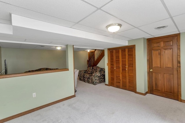 finished below grade area with carpet flooring, a paneled ceiling, baseboards, and stairs