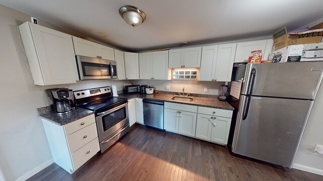 kitchen with dark stone counters, sink, white cabinets, stainless steel appliances, and dark hardwood / wood-style flooring