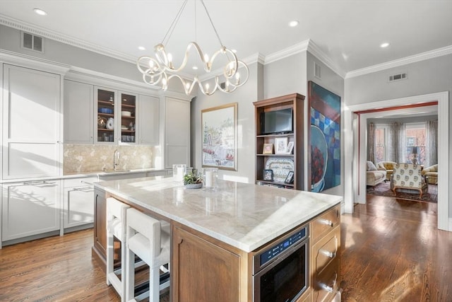 kitchen featuring light stone countertops, a kitchen island, white cabinetry, backsplash, and ornamental molding