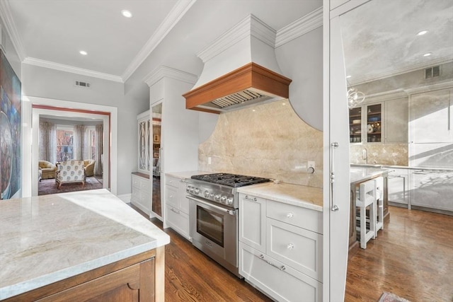 kitchen featuring high end stainless steel range, white cabinets, backsplash, light stone counters, and custom range hood