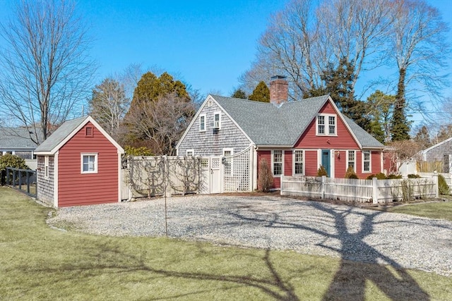 view of front of home featuring a fenced front yard, an outdoor structure, roof with shingles, a chimney, and a front yard