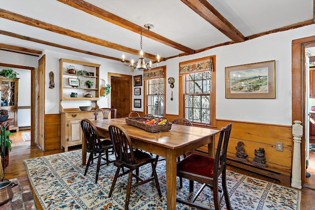 dining space with wood walls, a chandelier, beam ceiling, and wainscoting