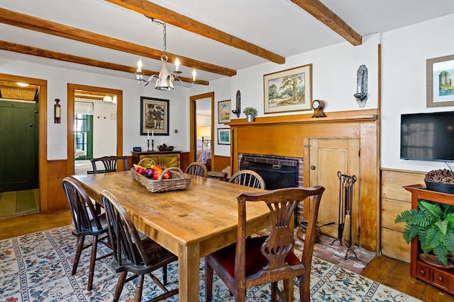 dining space with wooden walls, beam ceiling, wood finished floors, and wainscoting