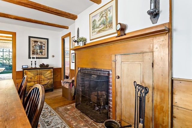 interior space featuring a brick fireplace, beamed ceiling, and a wainscoted wall