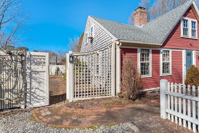 view of side of property featuring a chimney, fence, and roof with shingles