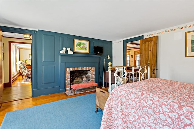 bedroom with a baseboard heating unit, a brick fireplace, and light wood-style floors