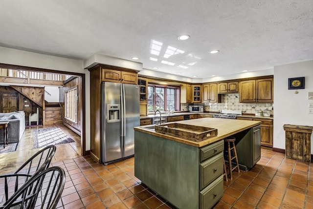 kitchen with backsplash, wooden counters, a kitchen island, glass insert cabinets, and appliances with stainless steel finishes