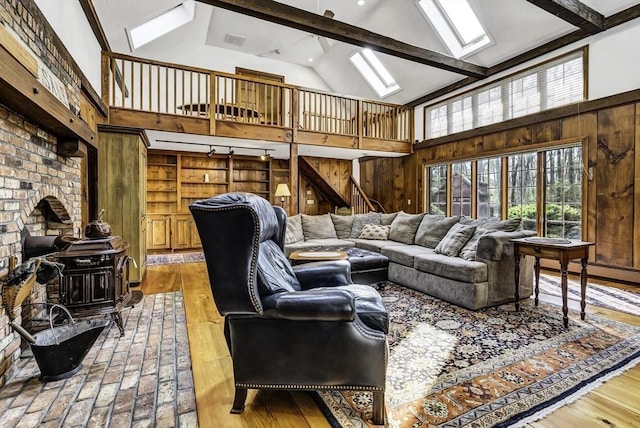 living area featuring a skylight, beamed ceiling, a wood stove, and wood walls