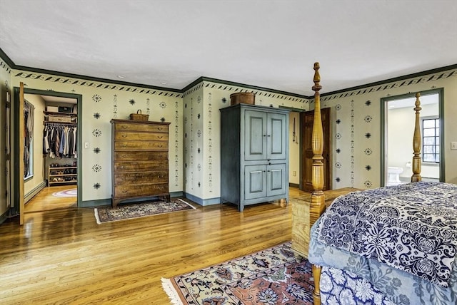 bedroom featuring a walk in closet, baseboards, ornamental molding, baseboard heating, and light wood-style flooring