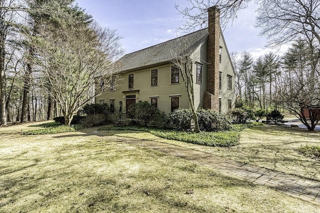 exterior space featuring a lawn, a chimney, and a shingled roof