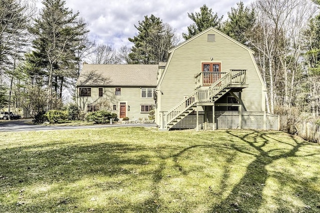 rear view of property with stairway, fence, roof with shingles, a gambrel roof, and a lawn