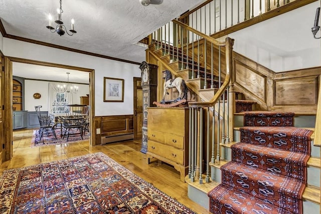 stairway with a wainscoted wall, an inviting chandelier, ornamental molding, wood-type flooring, and a textured ceiling