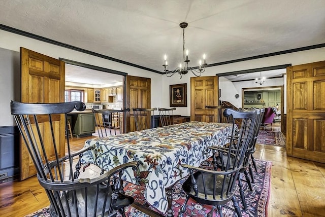 dining room featuring light wood finished floors, a notable chandelier, a textured ceiling, and crown molding