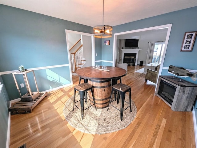 dining room with baseboards, a glass covered fireplace, stairway, an inviting chandelier, and light wood-style floors