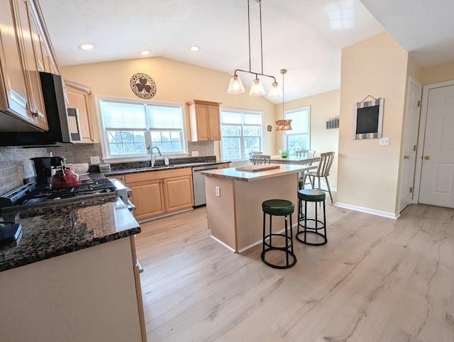 kitchen with lofted ceiling, stainless steel dishwasher, light brown cabinets, a kitchen island, and a kitchen breakfast bar